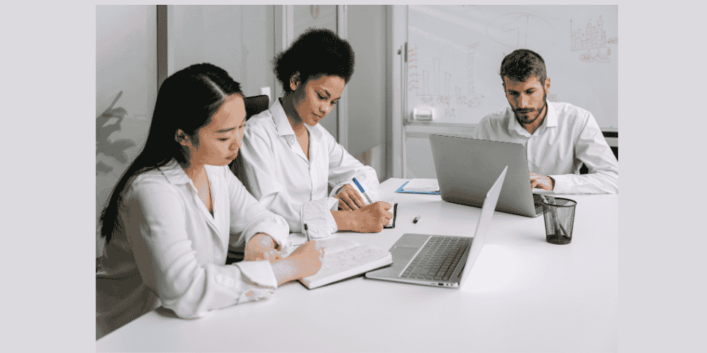 Professional team meeting with diverse colleagues working on laptops in modern office workspace"